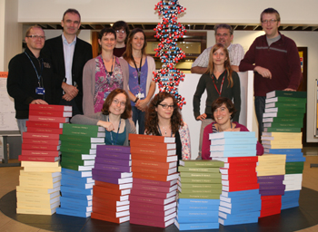 Ricercatori dell'Università di Leicester posano con una copia del genoma umano stampato su carta, in vari volumi.